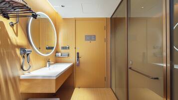 Un baño moderno con tocador de madera, un espejo con luz, zona de ducha y puerta de cristal.