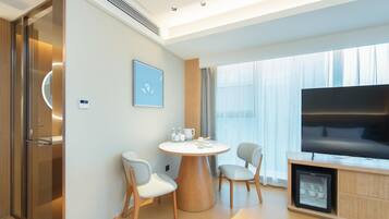 Habitación de hotel moderna con una mesa de comedor redonda, dos sillas, un televisor de pantalla plana y un minibar.