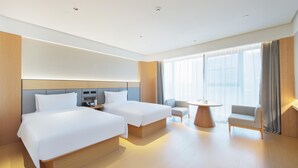 Habitación de hotel con dos camas, una mesita pequeña, una silla y un ventanal con cortinas.