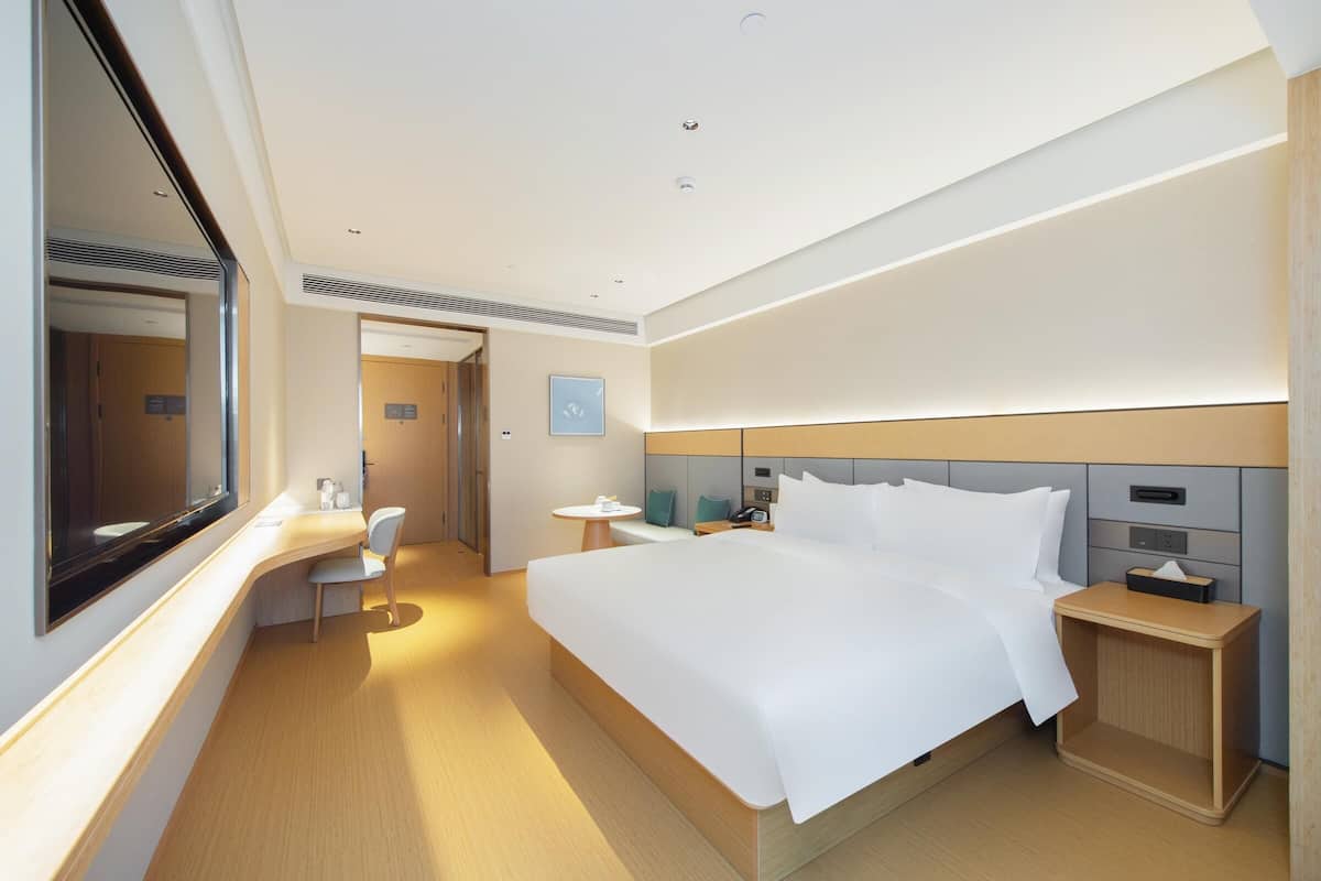 A modern hotel room with a large bed, bedside tables, a desk, and a chair.