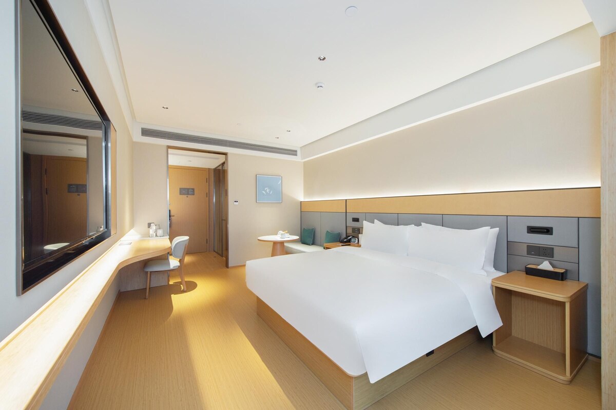 Ett modernt hotellrum med en stor säng, sängbord, ett skrivbord och en stol.