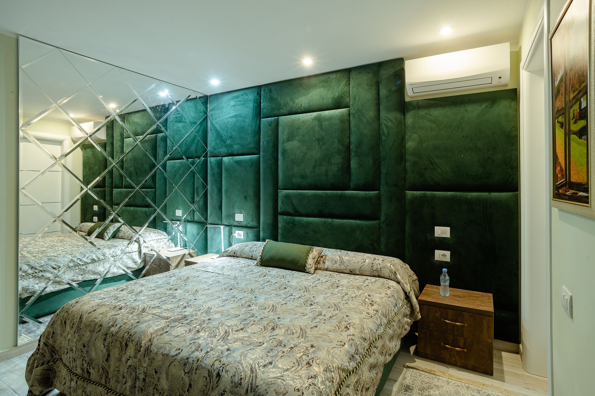 Un dormitorio moderno con una cama grande, un espejo y un cabecero tapizado en verde.