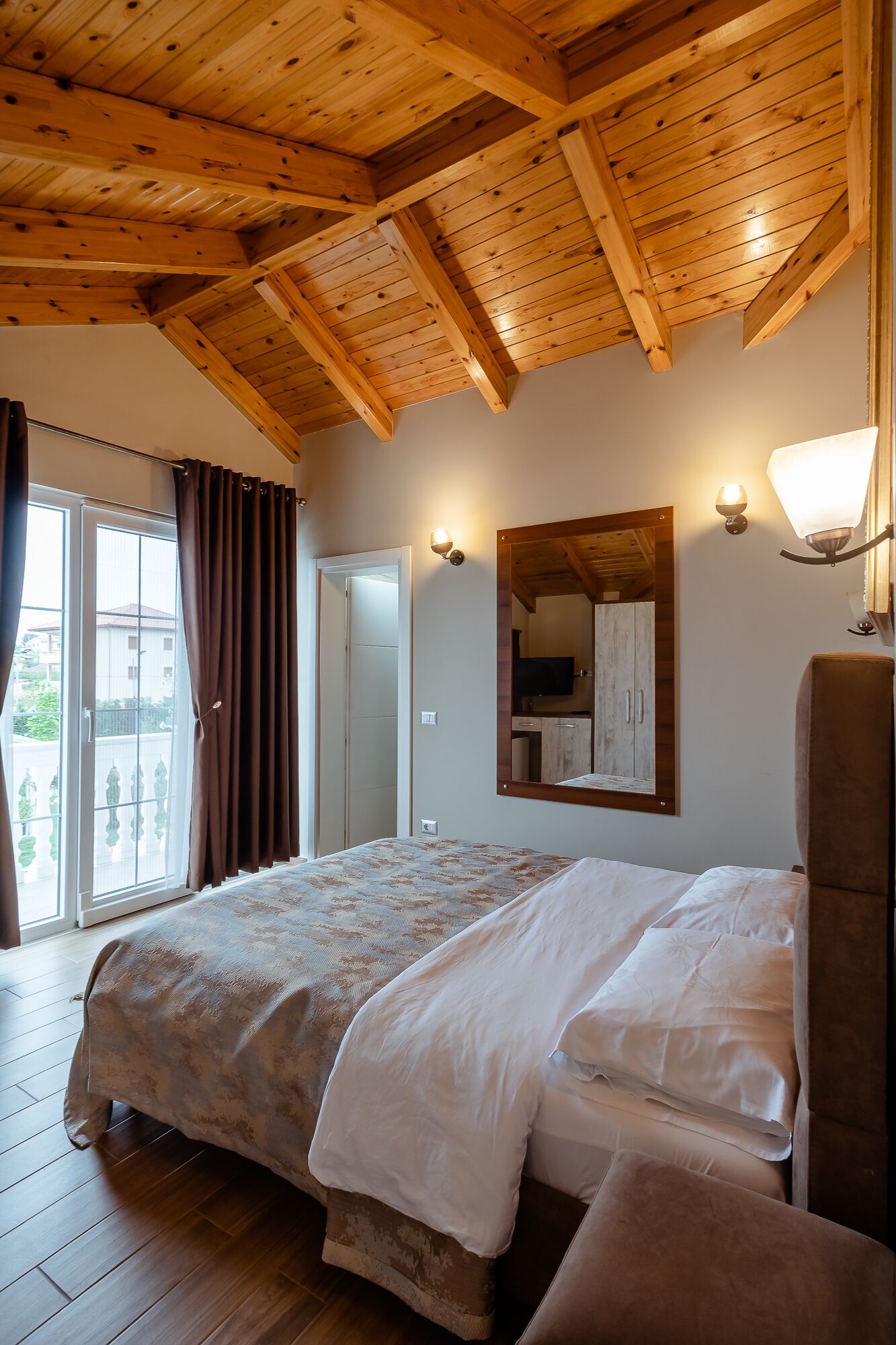 A bedroom with a wooden ceiling, a bed with a patterned bedspread, a large mirror, and a chair.