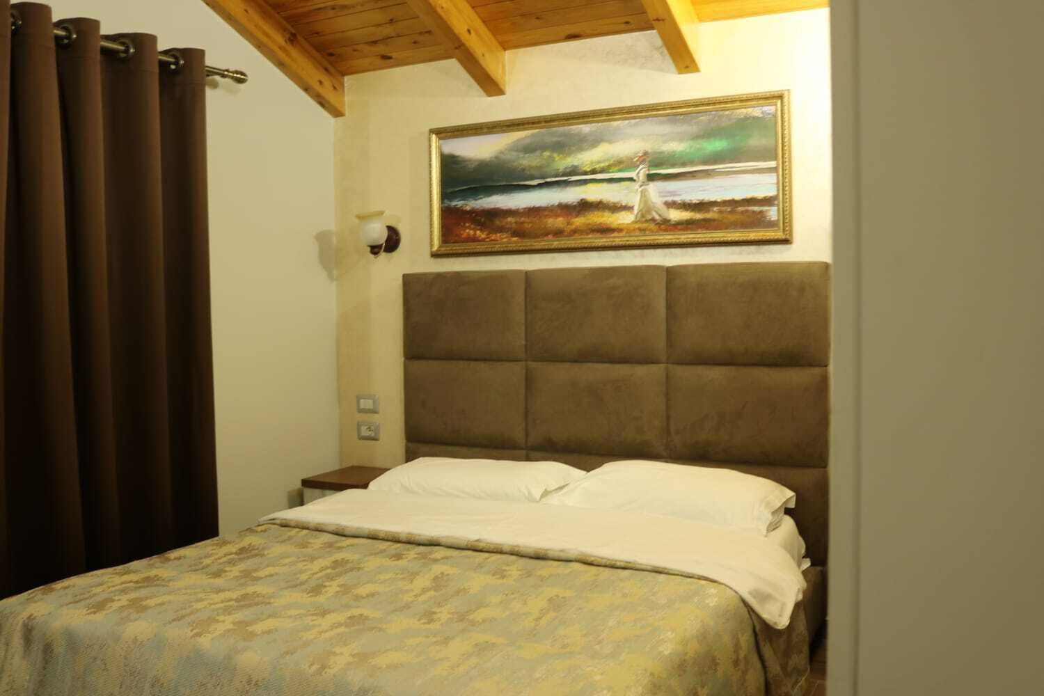 A bedroom with a large bed, a headboard, a painting on the wall, and a window with curtains.