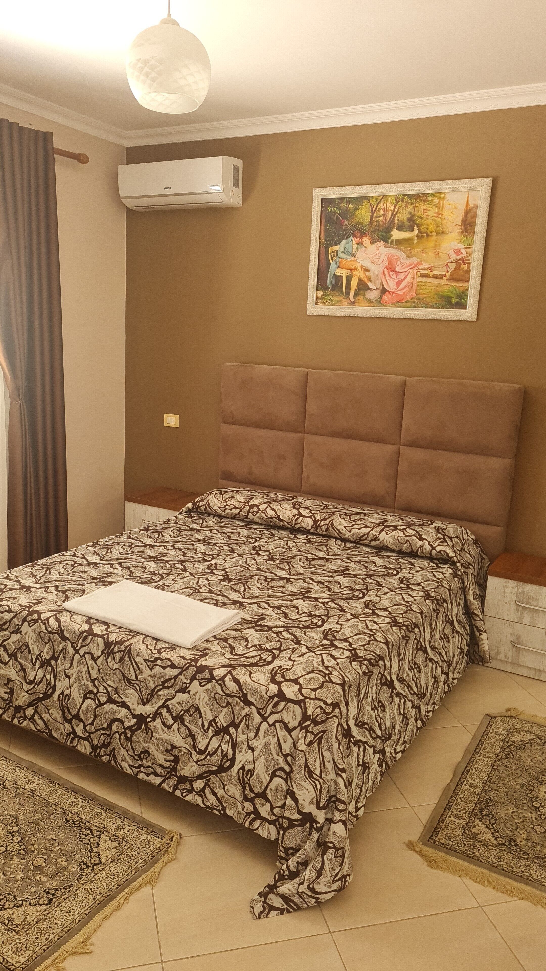 Una camera da letto con un letto, un quadro, un condizionatore e una finestra con tende.