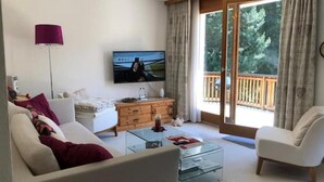 Ein modernes Wohnzimmer mit einer Couch, einem Glastisch, einem Fernseher und einem Holzschrank.