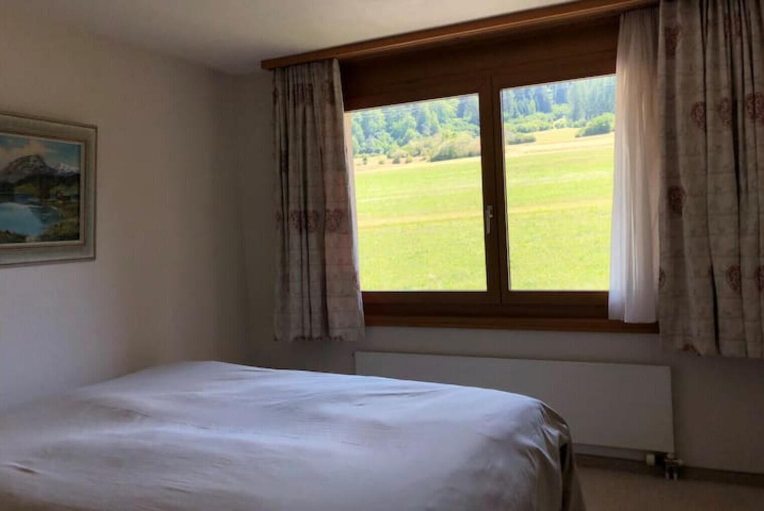 Un dormitorio con una cama individual, una ventana con cortinas y un cuadro en la pared.