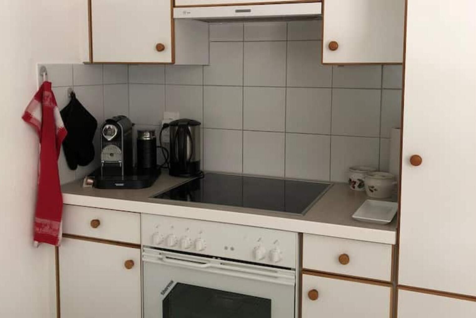 Une cuisine compacte équipée d’une cuisinière, d’une machine à café et d’une bouilloire posées sur le plan de travail.
