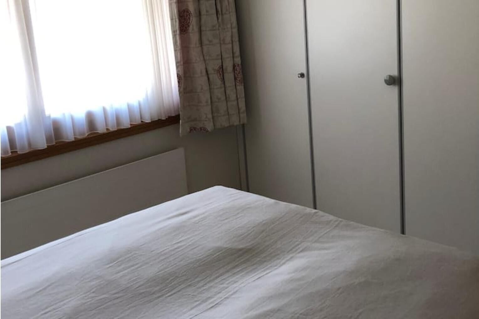 A bedroom with a bed, a window with curtains, and a wardrobe.