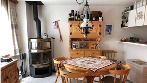 Eine gemütliche Küche mit Holzofen, Holzstühlen, einem Tisch mit Blumenmuster und Regalen mit Flaschen und Gläsern.