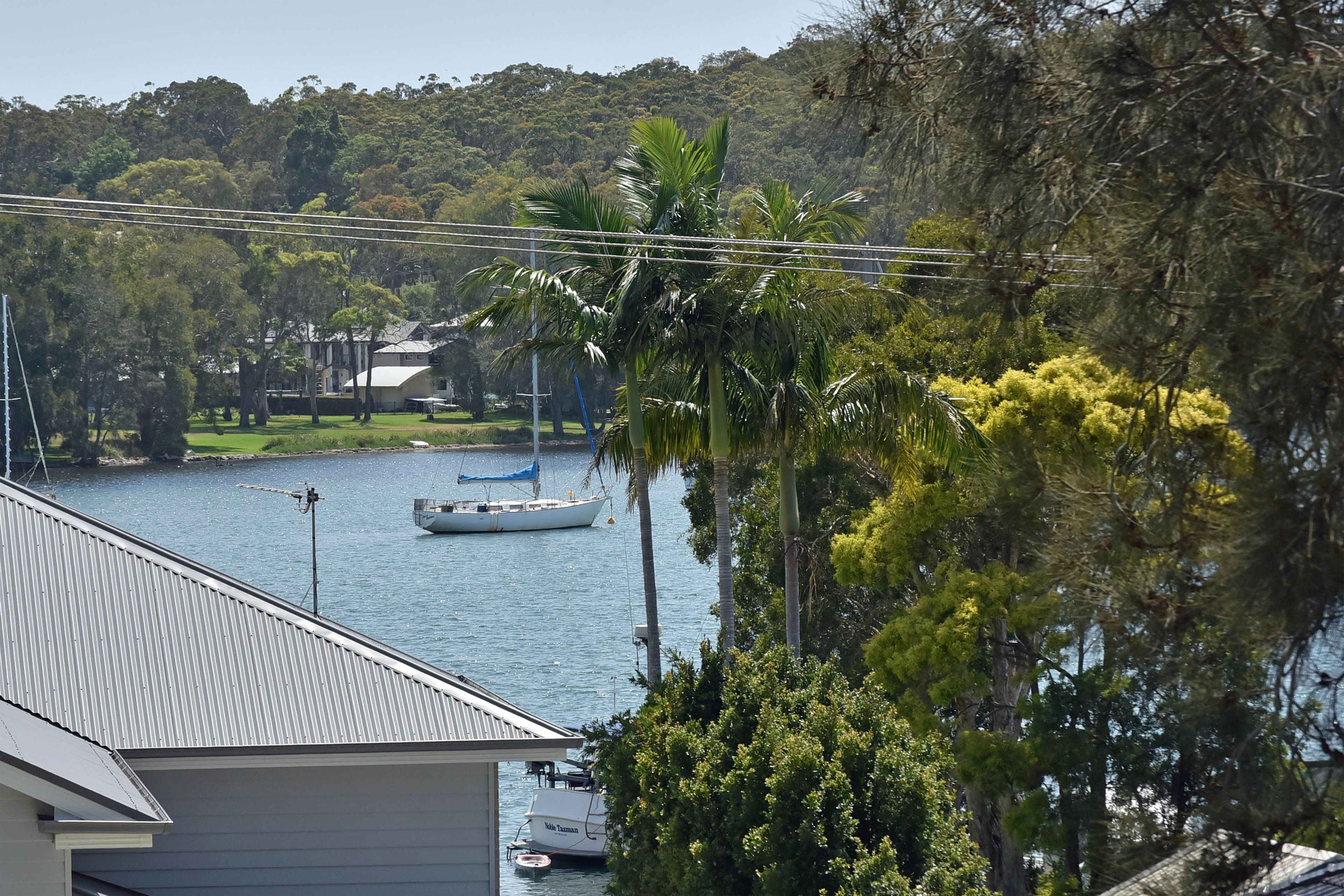 A residential area with a view of a lake, a sailboat, and a house with a metal roof.