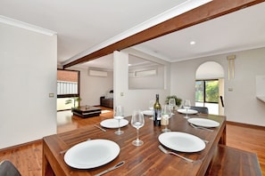 A dining area with a wooden table set for four, surrounded by white walls and a high ceiling with exposed beams.