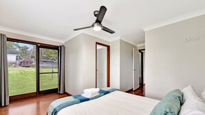 Une chambre avec un lit, un ventilateur de plafond, une vue à travers une porte-fenêtre coulissante et une porte donnant sur une autre pièce.