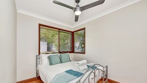A bedroom with a bed, a ceiling fan, and a window with blinds. - Breezy Bayside Haven at Brightwaters (Brightwaters)