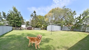 A backyard with a dog, fenced areas, and trees. - Breezy Bayside Haven at Brightwaters (Brightwaters)