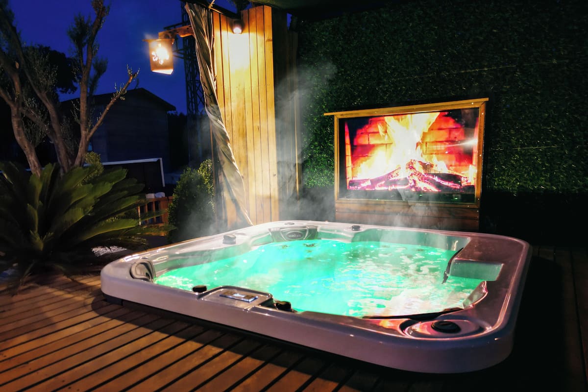 A hot tub on a wooden deck with a fire display in the background.