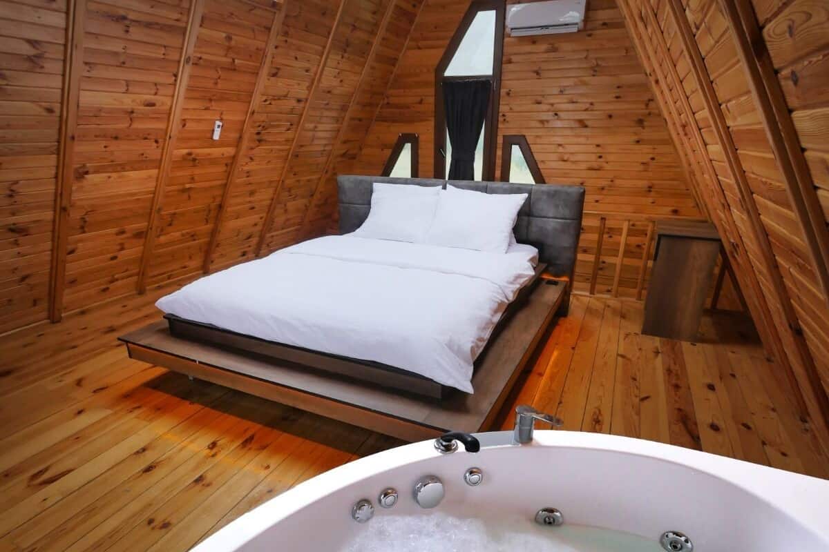 A wooden room with a bed, a large window, and a hot tub.