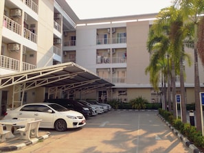A multi-story parking garage with several cars parked, a covered walkway, and a building with balconies.
