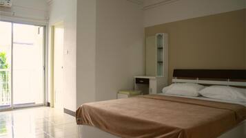 A hotel room with a bed, a bedside table, a mirror, and a sliding glass door leading to an outdoor area.