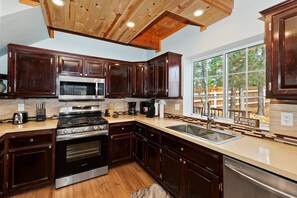 Une cuisine avec des meubles de couleur bois foncé, des appareils électroménagers en acier inoxydable et une grande fenêtre donnant sur les arbres.