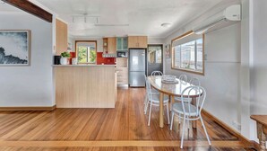 A modern kitchen with wooden cabinets, a central island, and a dining area with white chairs.