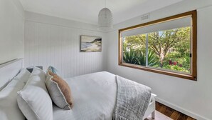 A bedroom with a bed, a large window with a view of greenery, a hanging light fixture, and a painting on the wall.