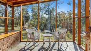 Un patio techado con mobiliario de mimbre y un muro de ladrillo.