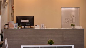 A reception desk with a computer, a fan, a calendar, and informational signs. - Thapae60 Mini Hotel (Chiang Mai)