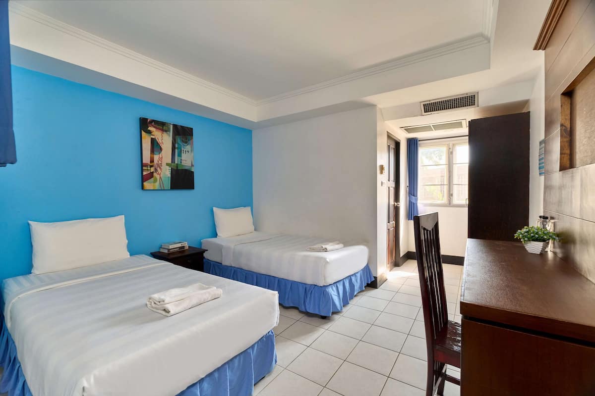 Habitación de hotel con dos camas, un escritorio y una silla. Hay un cuadro en la pared y una ventana con cortinas.