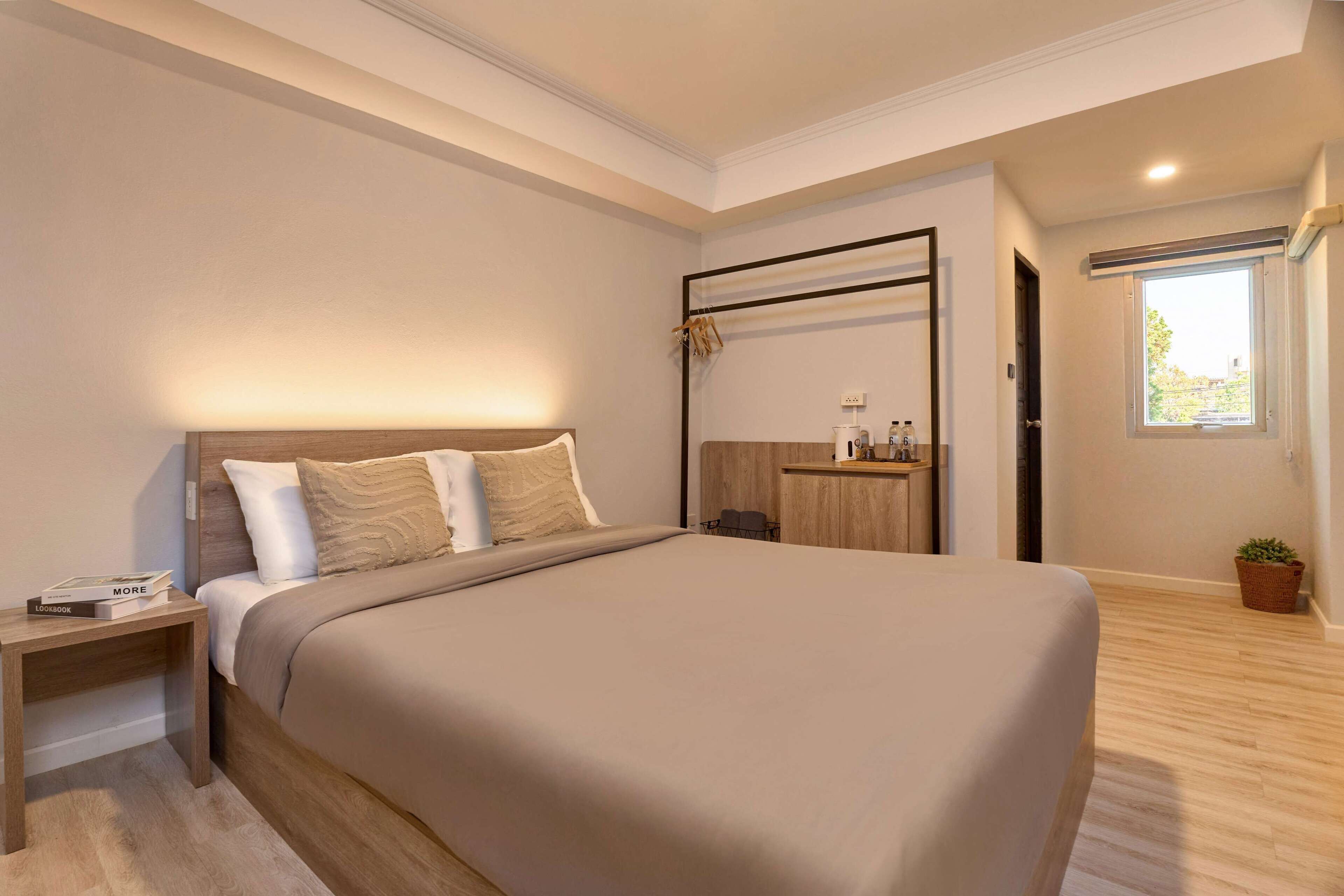 A modern bedroom with a large bed, a bedside table, a small desk, and a window with a view.