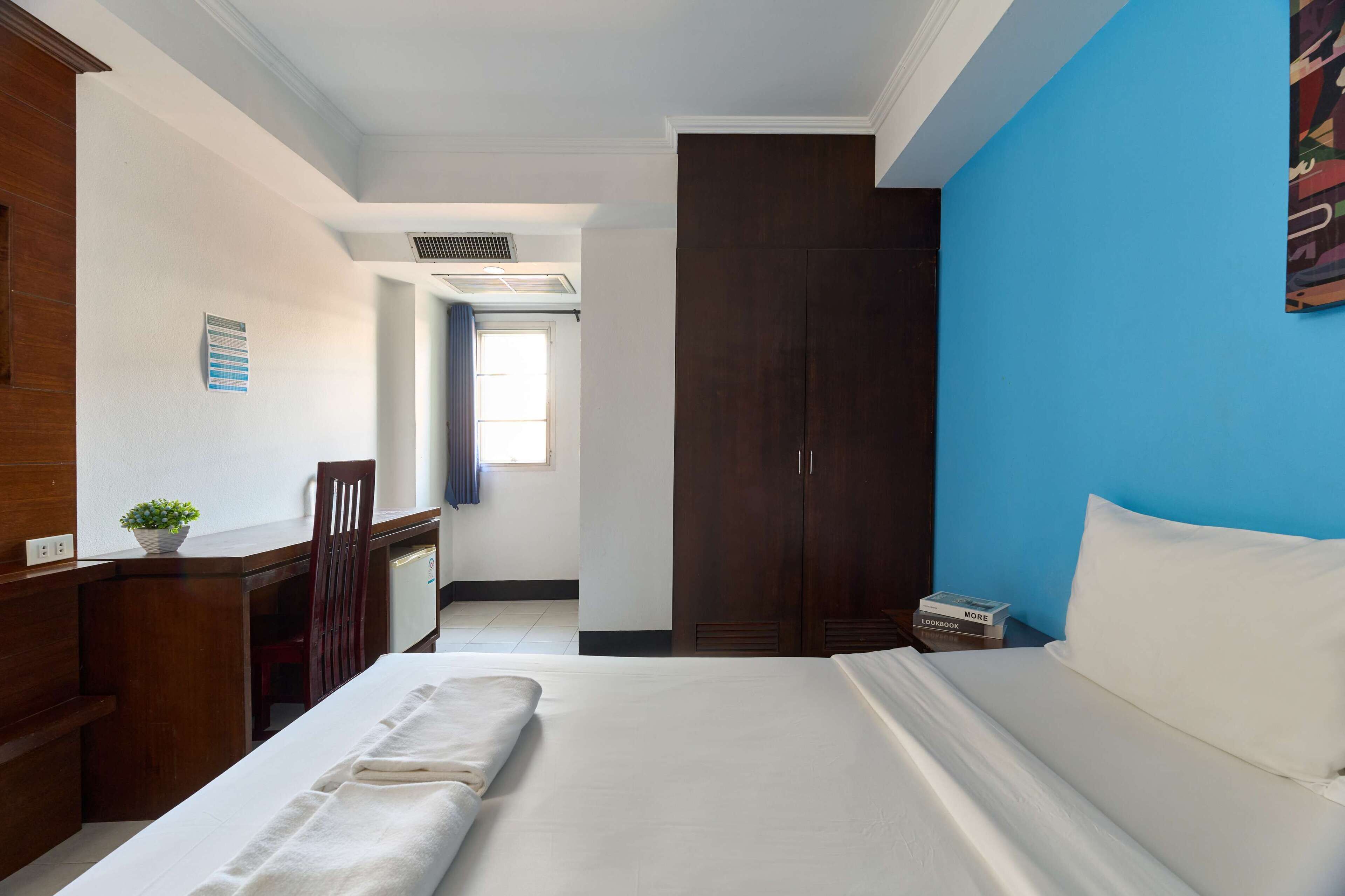 Una habitación de hotel con cama, escritorio, silla, armario y ventana.