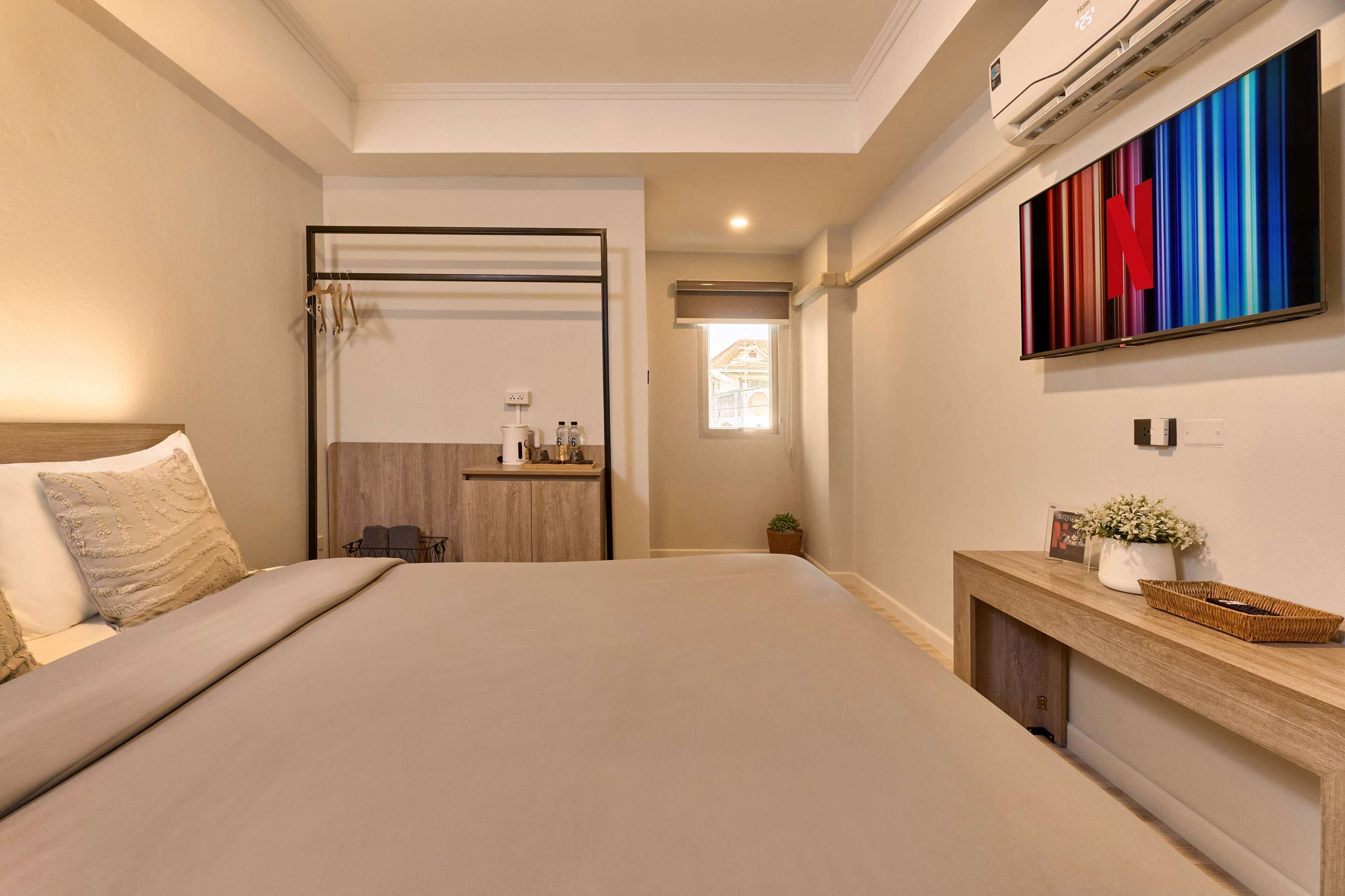 A hotel room with a large bed, a wooden console table, a TV mounted on the wall, and a view of the outside through a door.