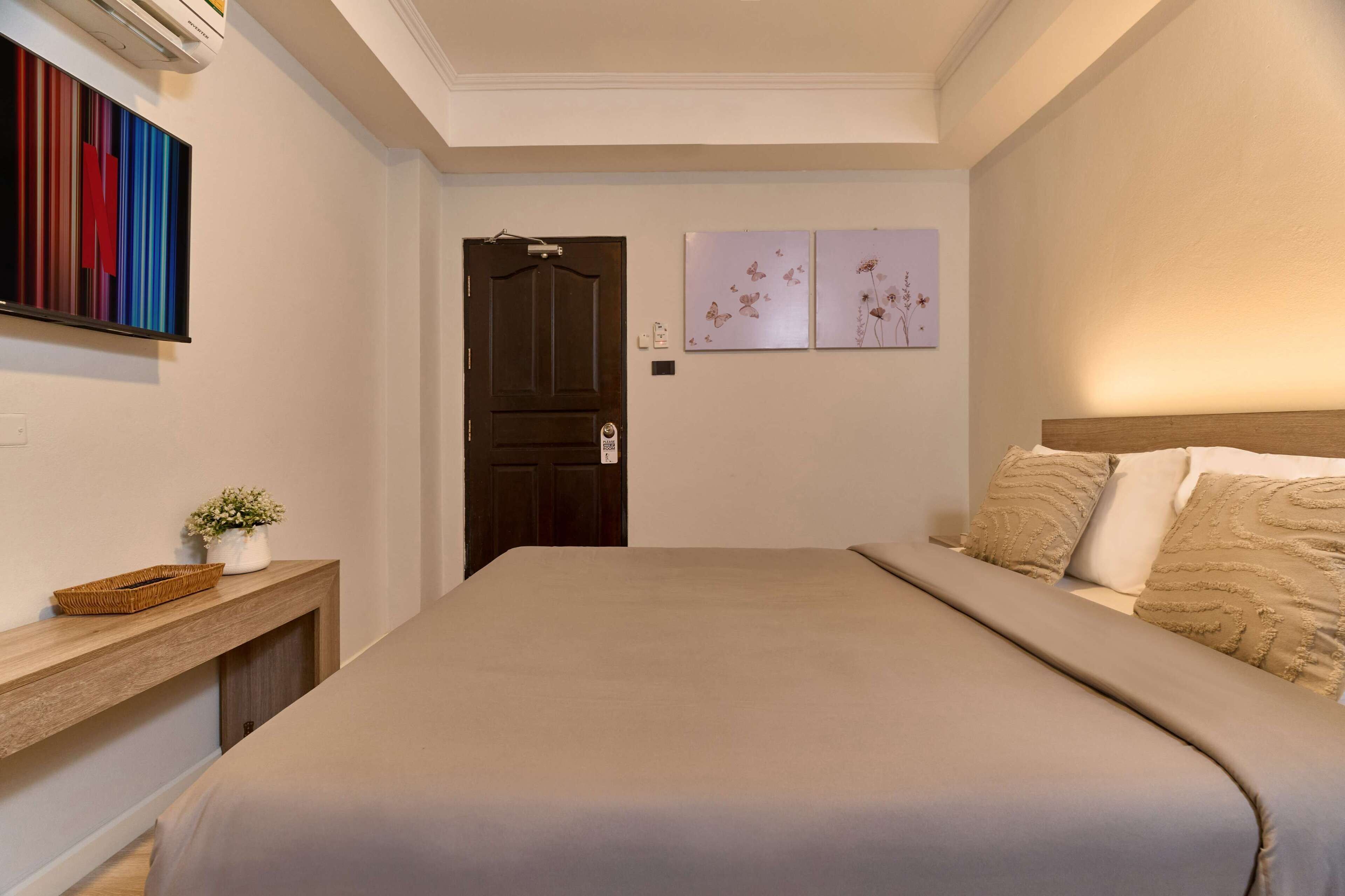 Un dormitorio ordenado con cama, una consola de madera, un televisor en la pared y dos obras de arte.