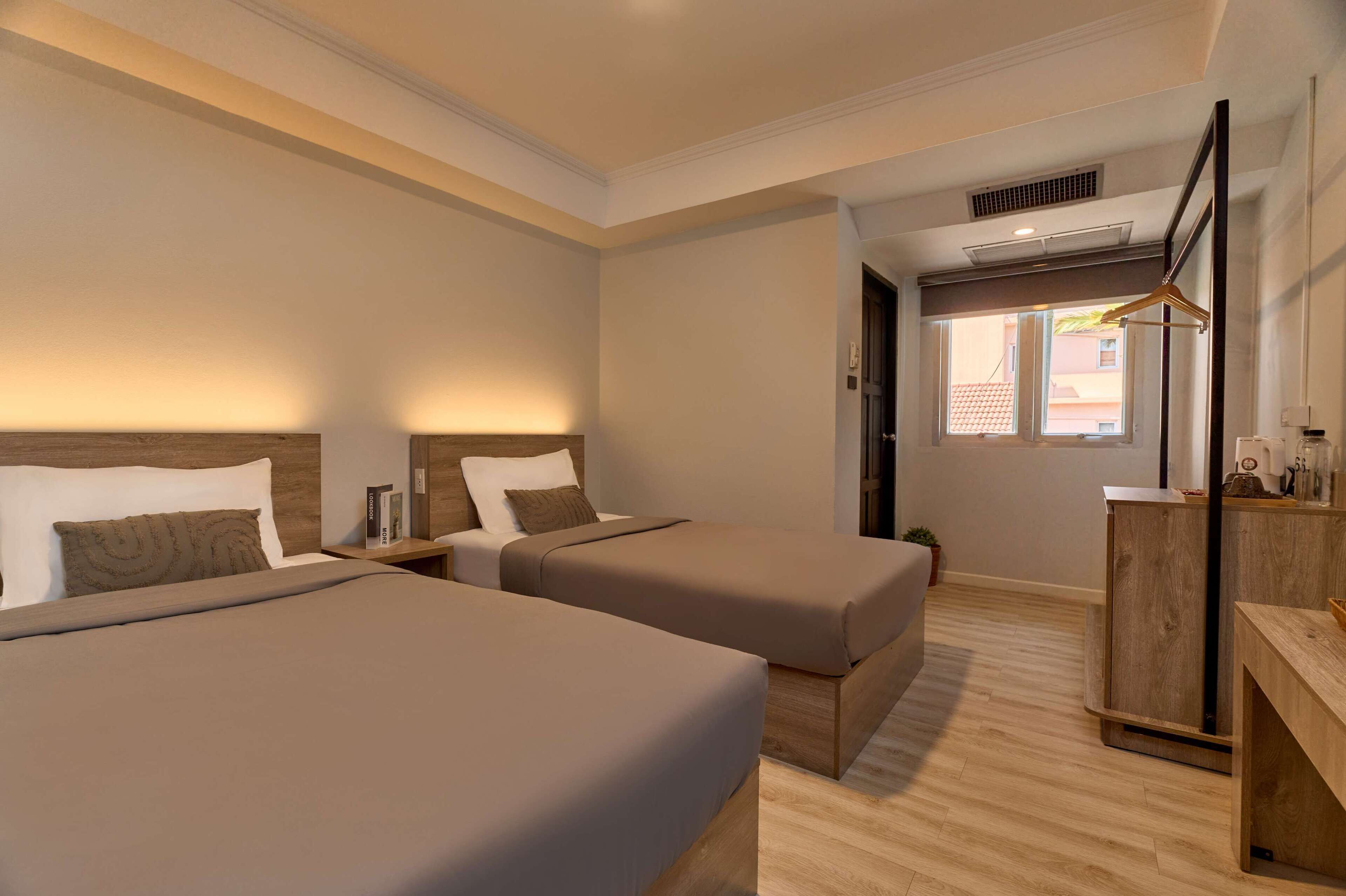 A hotel room with two beds, a wooden desk, and a window with a view of buildings.