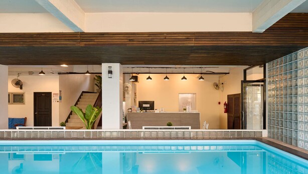 A swimming pool with a reception desk, a staircase, and a glass wall with a grid pattern. - Thapae60 Mini Hotel (Chiang Mai)