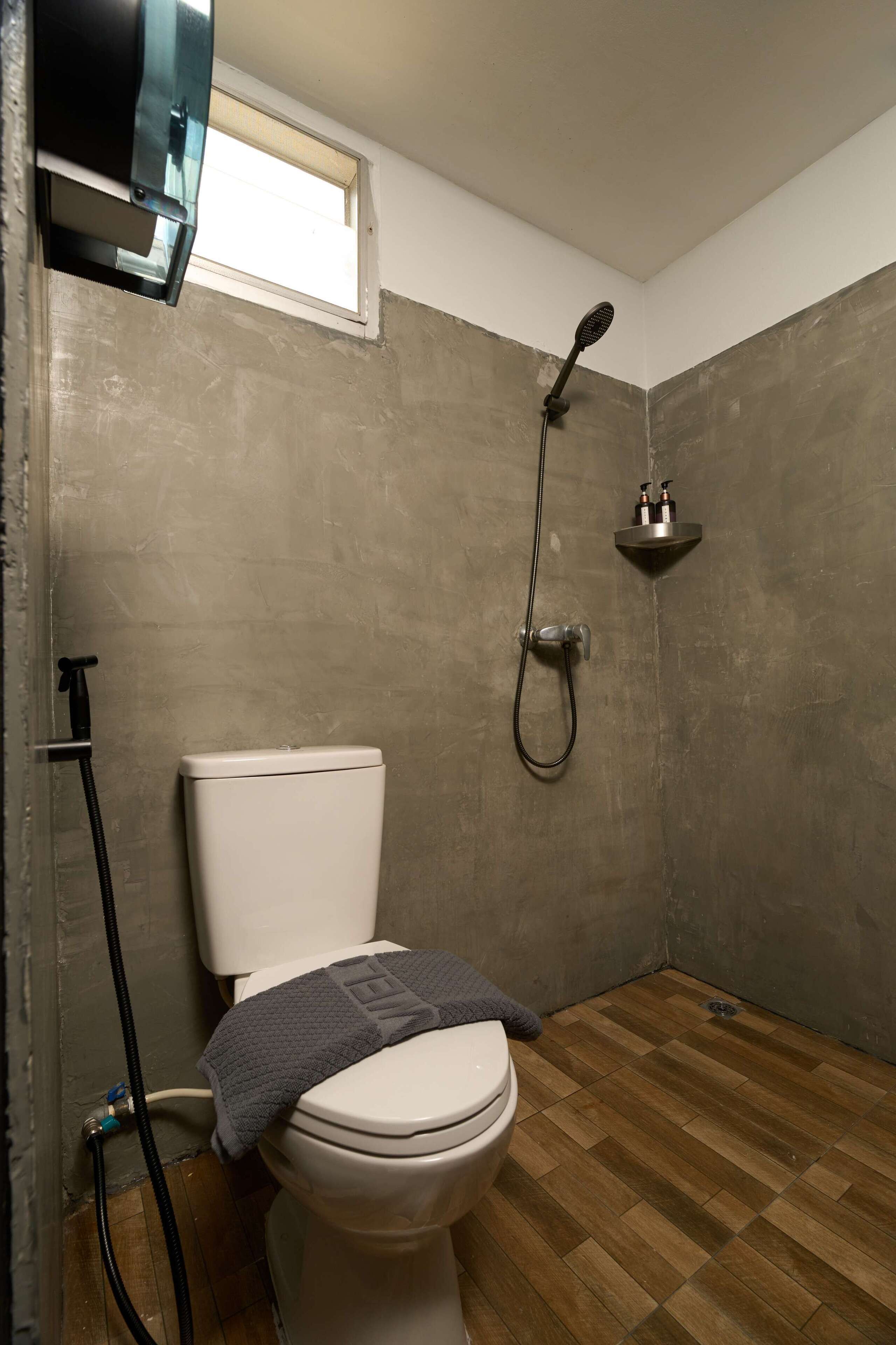 A bathroom with a toilet, shower, and a window.