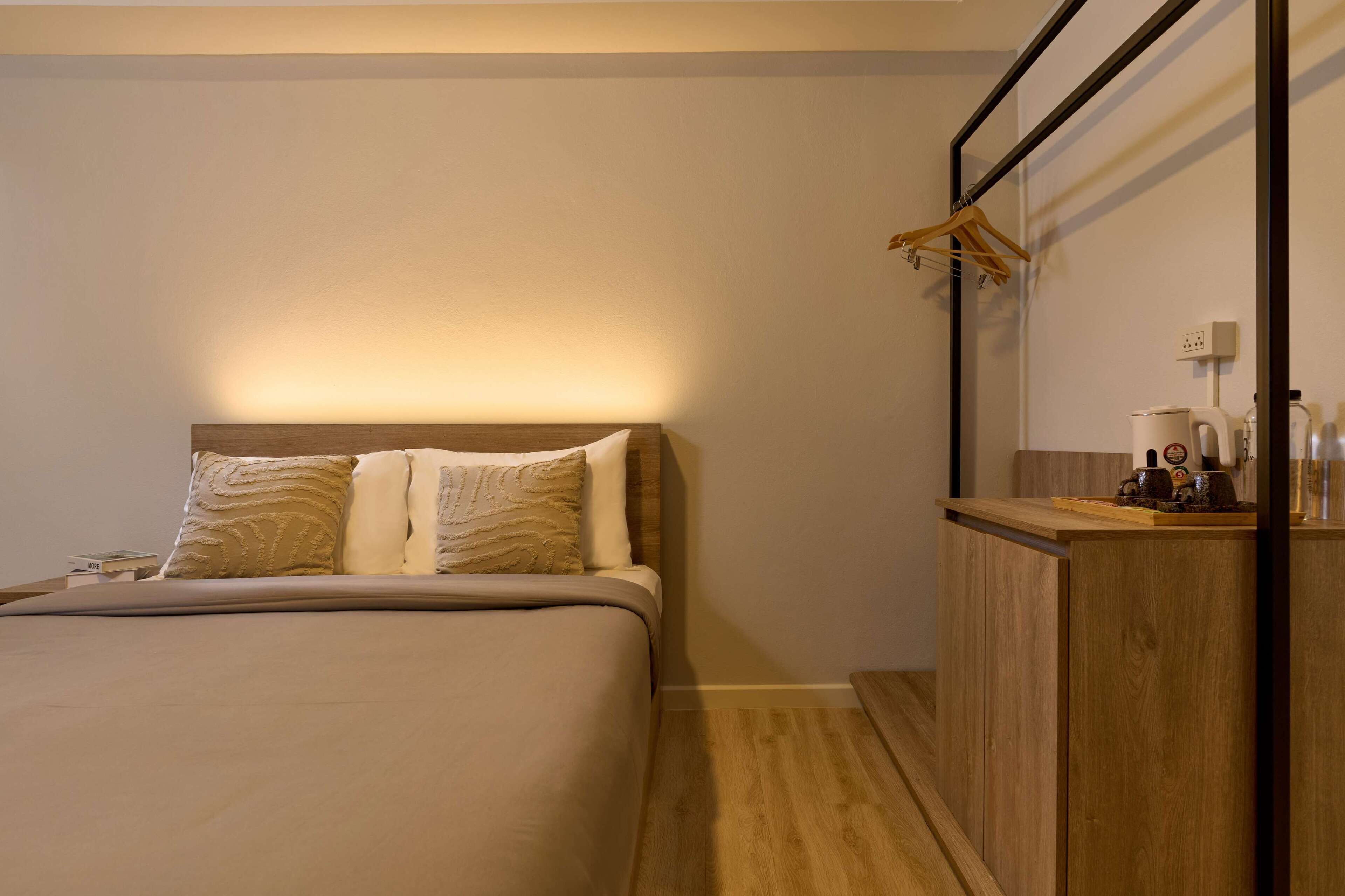 A neatly arranged hotel room with a bed, a wooden bedside table, a mirror, and a hanging coat rack.
