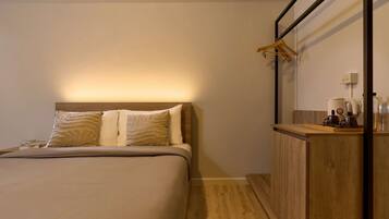 A neatly arranged hotel room with a bed, a wooden bedside table, a mirror, and a hanging coat rack.