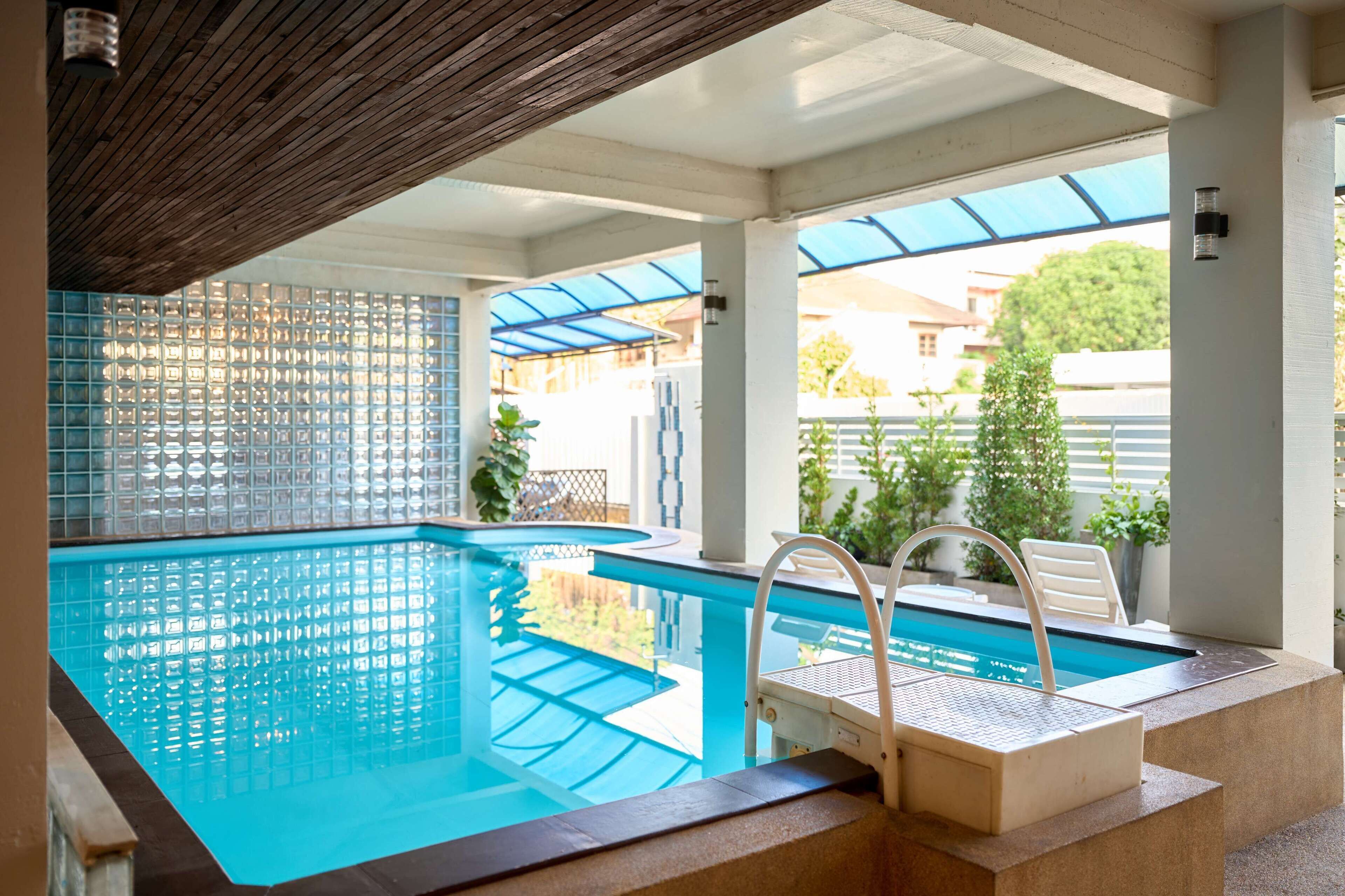 An indoor swimming pool with clear blue water, a wooden ceiling, and a view of the outside.