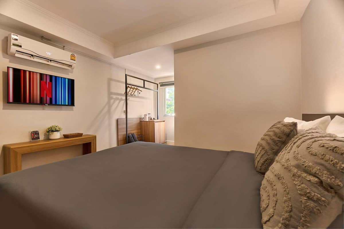 Un dormitorio moderno con una cama grande, una mesita de noche de madera con una planta, aire acondicionado de pared y una obra de arte colorida.