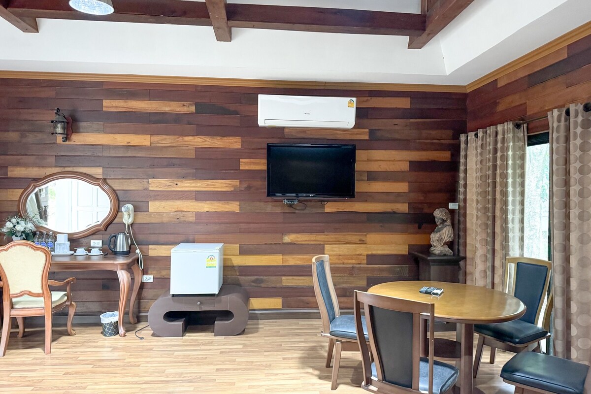 A room with wooden panel walls, a flat-screen TV, a wooden dining table with chairs, a small white heater, and a mirror.
