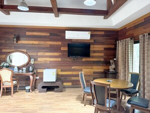 A room with wooden panel walls, a flat-screen TV, a wooden dining table with chairs, a small white heater, and a mirror.