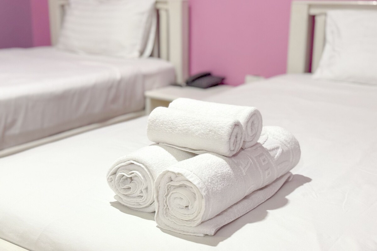 A hotel room with two beds, a nightstand, and a rolled white towel on the bed.