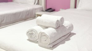 A hotel room with two beds, a nightstand, and a rolled white towel on the bed.