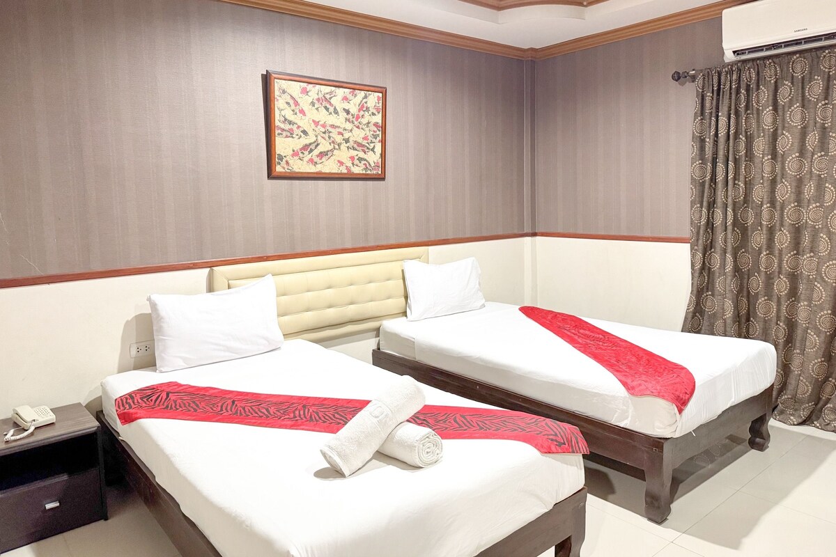 A hotel room with two beds, a telephone on the nightstand, a wall-mounted air conditioner, and a patterned curtain.