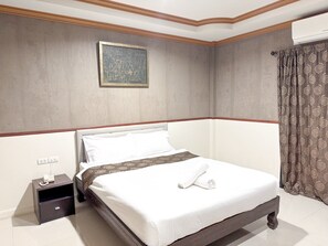 A neatly made bed with white linens, a bedside table with a phone, and a patterned curtain. - Grand Amazon Hotel by Zuzu (Lampang)