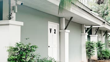 A building with a white exterior, a door labeled 'V2', and a small garden area with greenery.