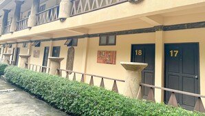 A building with numbered doors, a balcony with railings, and a hedge in front.