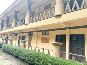 A building with numbered doors, a balcony with railings, and a hedge in front.