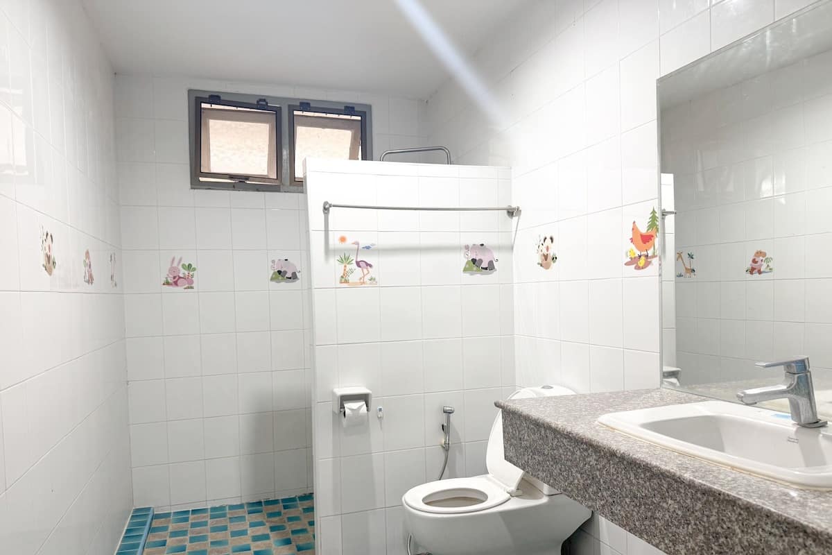 A bathroom with white tiles, a toilet, a sink, and a window.
